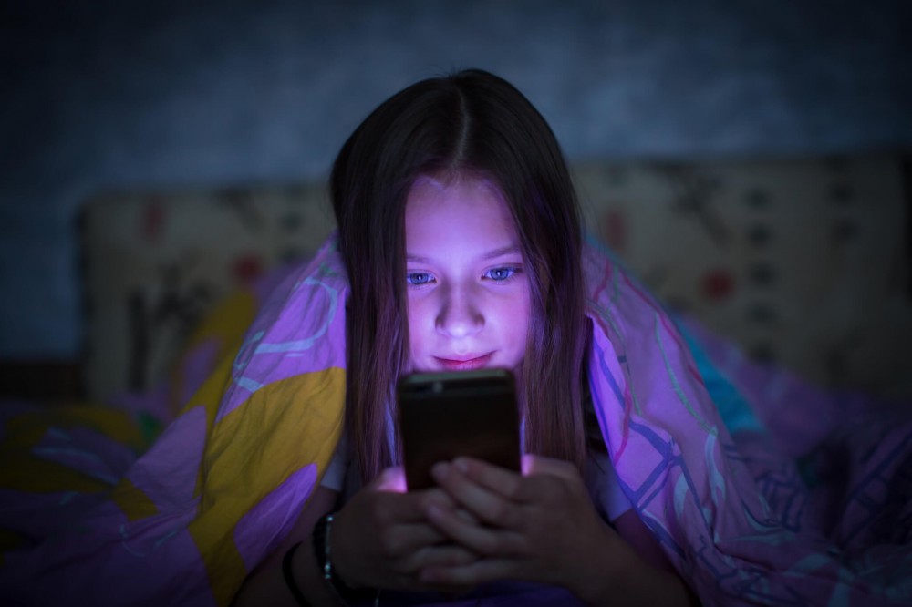 Teen girl in bed looking at smartphone at night